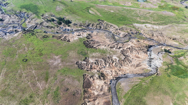 Aerial view of severe soil erosion and deep gullies cutting through green grassy hills and a winding stream bed in Pietermaritzburg, KwaZulu-Natal, South Africa.