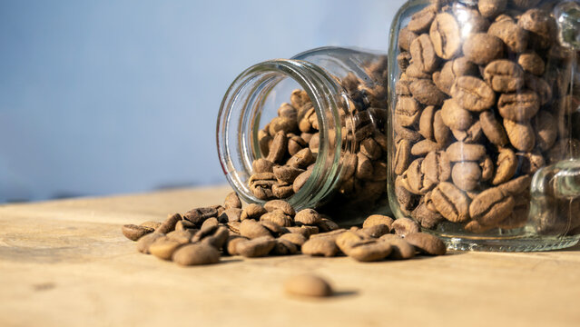 Whole Coffee Beans Pouring from Tilted Glass Mug on Wooden Surface
