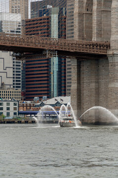 Fireboat Spraying Water Under Brooklyn Bridge. Vertical shot of a fireboat spraying water near the stone pylon of Brooklyn Bridge.