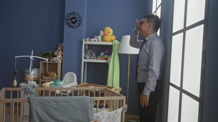 Man in building stands by a wooden crib and stuffed toys, adjusts glasses and rubs forehead while holding frames  fatigue care. © Krakenimages.com