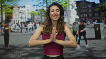 Fototapeta premium Young woman wearing red tank top makes ok sign with fingers in bright city street under sunlight; serenity calm peace tranquility.