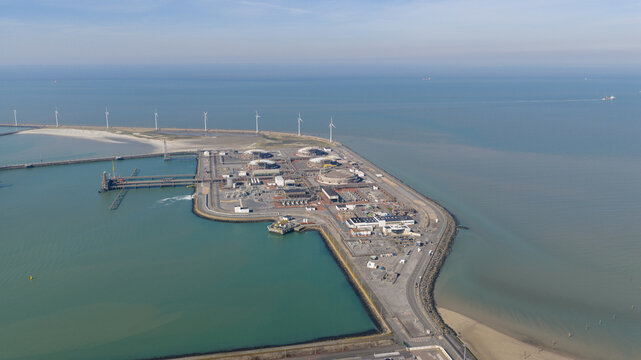 Aerial view of the Fluxys - LNG Terminal Zeebrugge featuring industrial storage tanks and coastal wind turbines along the North Sea in Brugge, Vlaanderen, Belgium.