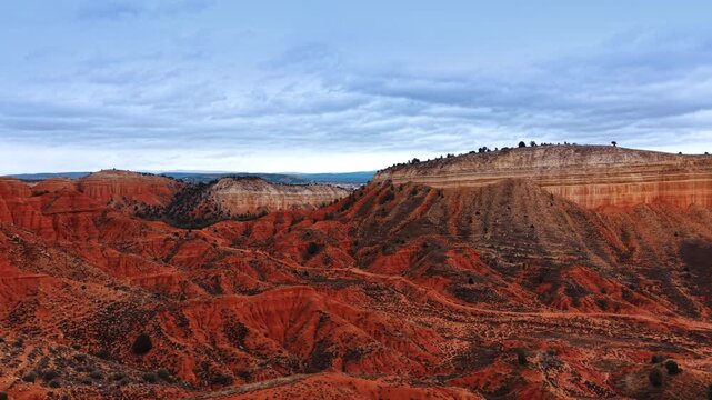 Footage over rocky red landscape with scarce vegetation growing on. Thick cloudscape covers the sky over the scenery. Teruel, Spain.