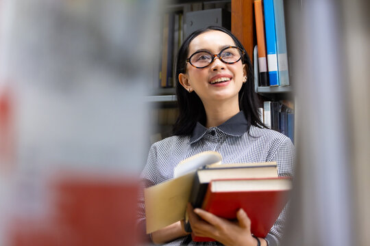 Young Asian woman studies in quiet library. Books line tall shelves behind. she holds  book, eyes focused. Serene atmosphere, calm concentration. Ideal for educational or study-themed projects