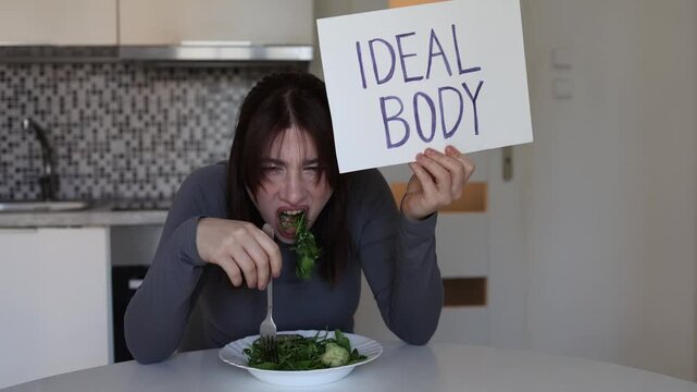 Young woman aggressively chasing ideal body standards while forcing herself to eat healthy food showing obsession with appearance toxic beauty culture and dieting pressure