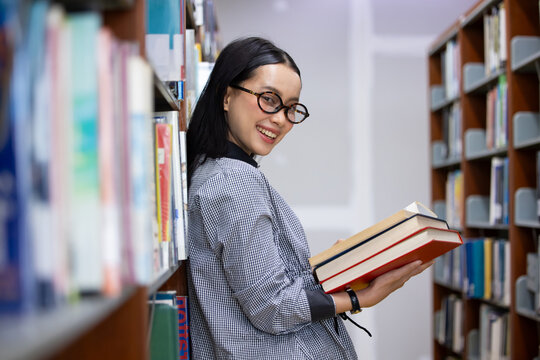 Young Asian woman studies in quiet library. Books line tall shelves behind. she holds  book, eyes focused. Serene atmosphere, calm concentration. Ideal for educational or study-themed projects