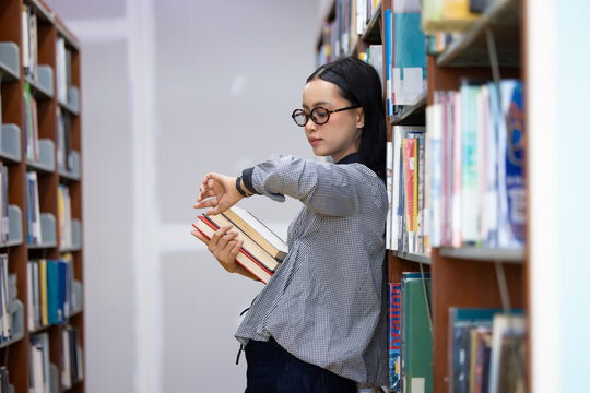 Young Asian woman studies in quiet library. Books line tall shelves behind. she holds  book, eyes focused. Serene atmosphere, calm concentration. Ideal for educational or study-themed projects