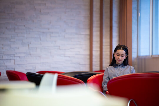 Young Asian woman studies reading book anf Siting on red chair in quiet library. Books line tall shelves behind. she holds book, calm concentration. Ideal for educational or study-themed projects