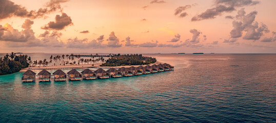 Breathtaking aerial view of Maldives water villas at sunset over a peaceful ocean luxury summer resort picturesque travel landscape wallpaper with serene turquoise sea and golden hour sky panorama © icemanphotos