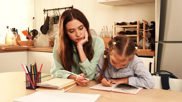 The mother sat at the dining table helping her daughter with her homework, while the daughter happily wrote in her notebook at home.