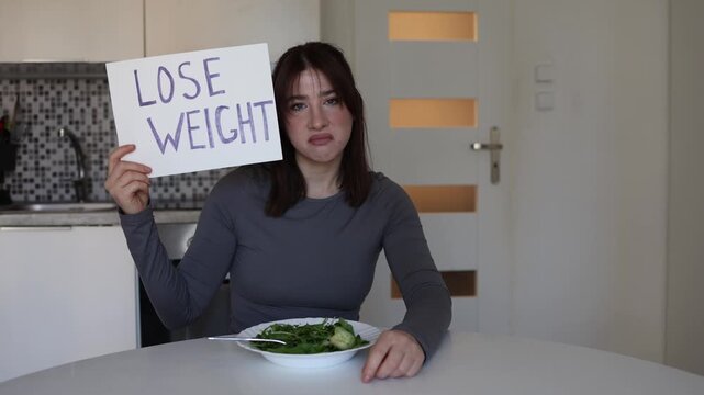 Young woman holds lose weight sign while eating salad criticizing toxic beauty standards social media pressure and obsession with unrealistic body ideals