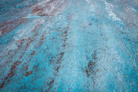 Close-up of a vibrant turquoise meltwater stream carving a winding path through the textured blue ice and moraine debris of an Alaskan glacier