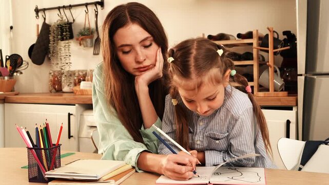 The mother sat at the dining table helping her daughter with her homework, while the daughter happily wrote in her notebook at home.
