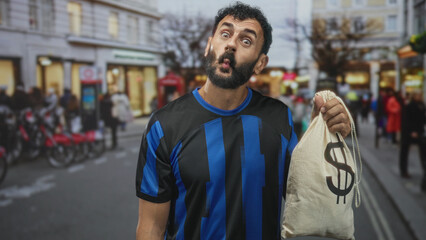 Fototapeta premium Man in soccer uniform smiling and holding a canvas money bag with dollar sign while standing on a busy urban street lined with shops and bicycles; confidence success.