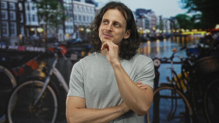 Fototapeta premium Man with hand on chin and closed eyes on amsterdam street by canal with bicycles and water reflections; thoughtful introspection.