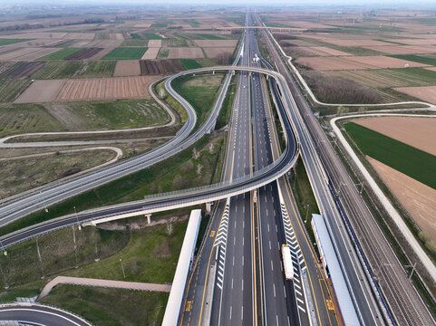 Aerial view of the A4 Torino-Milano motorway interchange with curved overpasses, surrounding agricultural fields, and a parallel railway line under a clear sky in Borgo d'Ale, Piedmont, Italy.