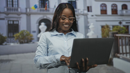 Woman wearing glasses typing on laptop with hands visible while standing at a public building...