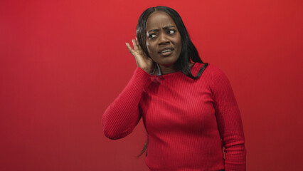 Obraz premium Woman cupping ear with hand listening carefully in studio red backdrop wearing ribbed red sweater; curiosity playfulness.