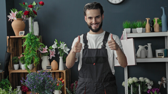 Man florist showing thumbs up with flowers, bouquets and vases in a building; friendly optimism service.