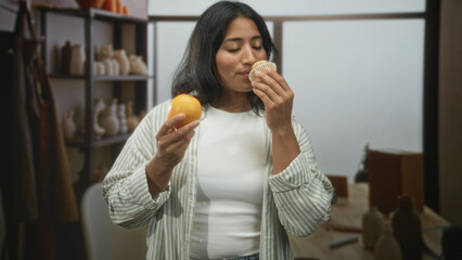 Woman smelling orange with nose close, eyes closed while holding muffin among ceramic vases on...