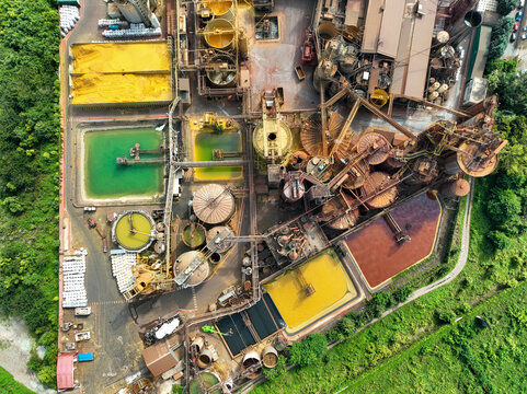 Aerial view of an industrial facility with large storage tanks, complex piping systems, and colorful settling ponds surrounded by green trees in Turin, Piedmont, Italy.