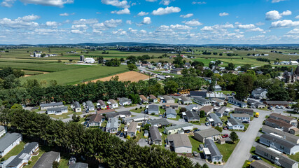Fototapeta premium Houses are arranged in a neighborhood surrounded by fields and trees. Bright sky with clouds adds to the scene. This shows a typical residential setup in a rural area.