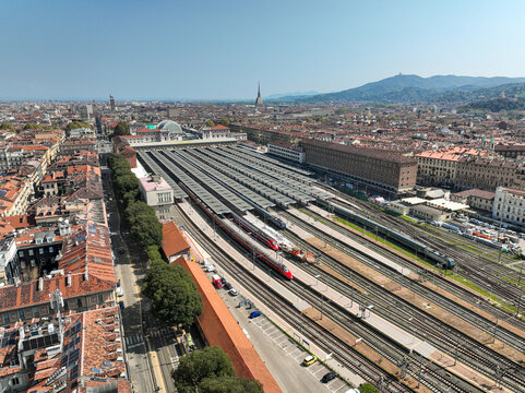 Aerial view of Porta Nuova railway station with trains on tracks, historic city buildings, and the Mole Antonelliana under a clear blue sky in Turin, Piedmont, Italy.
