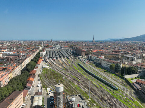 Aerial view of Porta Nuova railway station with numerous train tracks, platforms, and the urban skyline under a clear blue sky in Turin, Piedmont, Italy.