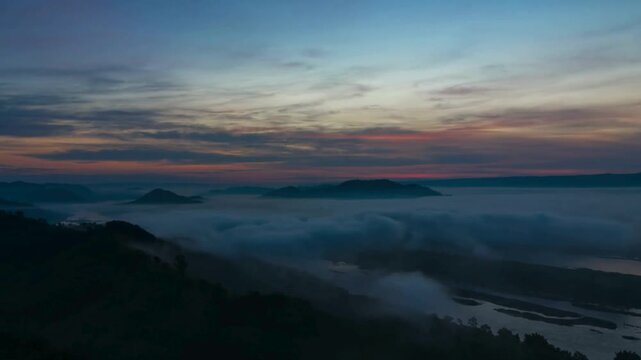 Breathtaking timelapse showing golden sunrise illuminating clouds above deep river valley surrounded by misty mountains during early morning calm scenery.