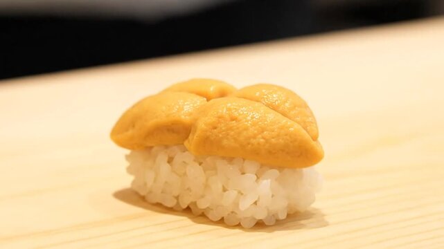Close-up of a chefs hands preparing fresh uni sushi, placing sea urchin roe on a bed of rice, showcasing the delicate process of making this Japanese delicacy.