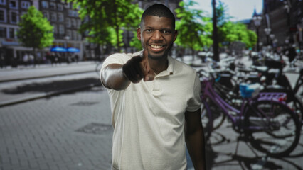 Fototapeta premium Man pointing finger and smiling toward camera on a busy street with parked bicycles and trees; connection joy.