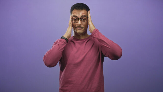 Man with glasses pressing hands to temples and then smiling in studio with purple backdrop; relief ease.