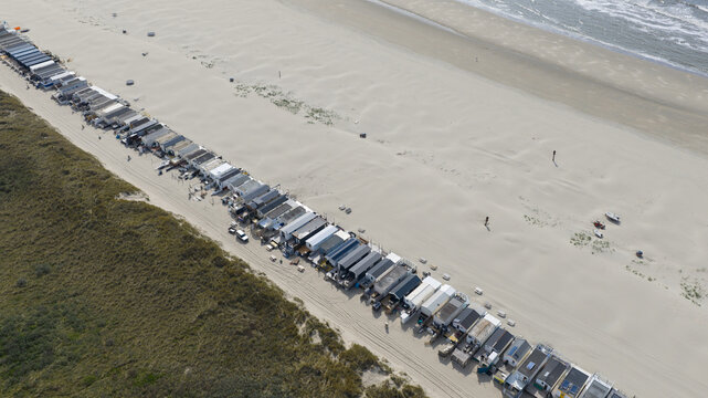 Aerial view of a long row of beach houses situated between grassy dunes and the sandy shoreline of the North Sea in Velsen-Noord, Noord-Holland, Netherlands.