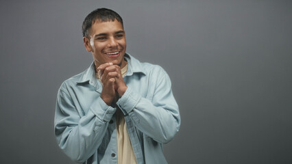 Fototapeta premium Man clasping hands and smiling in studio, wearing light blue denim shirt with visible hands and relaxed pose; happiness casual warmth.