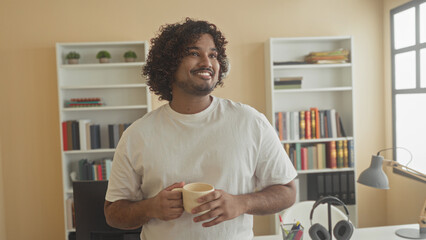 Man holds coffee cup with both hands and looks up at window in a building filled with bookshelves and desk  calm reflection. © Krakenimages.com