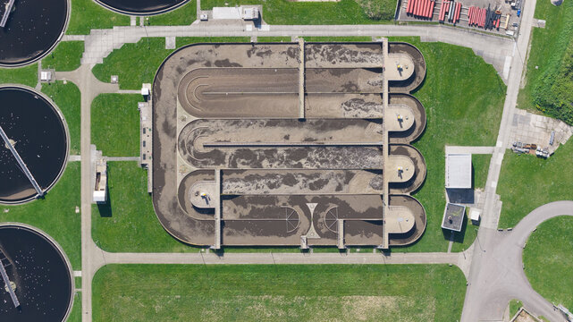 Aerial view of RWZI - Geestmerambacht wastewater treatment plant with circular aeration tanks, oval basins and industrial infrastructure.