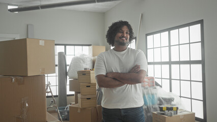 Man in white t shirt stands with arms crossed among stacked moving boxes, bubble wrap and ladder inside a new building interior  fresh start pride. © Krakenimages.com