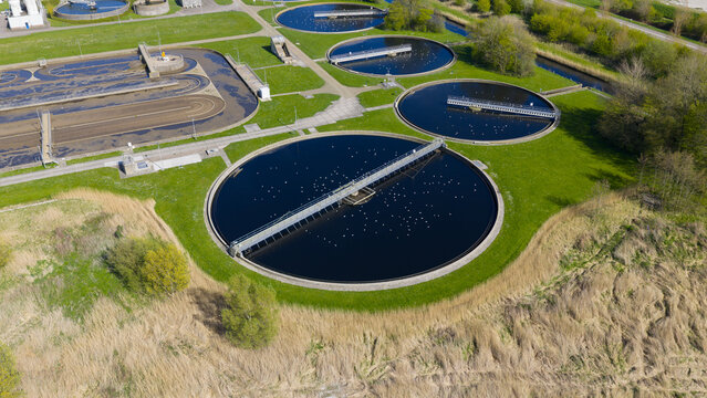 Aerial view of the circular clarifier tanks at the RWZI - Geestmerambacht wastewater treatment plant with rotating bridges and seagulls on the water in Netherlands.