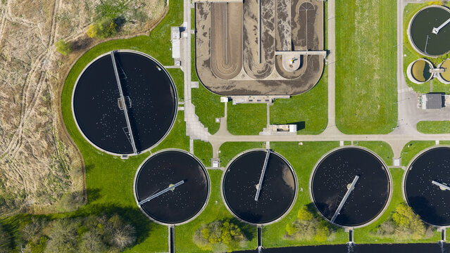 Aerial view of the RWZI Geestmerambacht wastewater treatment plant featuring circular clarifiers and rectangular aeration tanks surrounded by green lawns and trees.