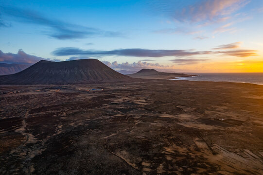 The scene captures Lanzarote and La Graciosa Canary Island at sunset, showcasing volcanic hills and coastline. The sun sets over the ocean, enhancing the landscape features.