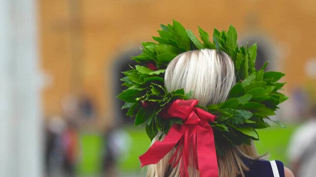 Graduated student posing with laurel crown in Piazza dei Miracoli under the Leaning Tower of Pisa