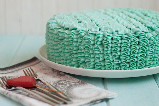 Close-up of a cake covered in green buttercream frosting on a wooden table with cutlery
