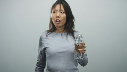 Woman holding a plastic water bottle to her temple with folded arm, pouting and frowning, wearing hoop earring and gray long sleeve top in studio  headache discomfort. © Krakenimages.com
