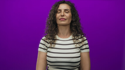 Obraz premium Hispanic woman wearing white striped shirt standing calmly with closed eyes in purple studio; inner calm.