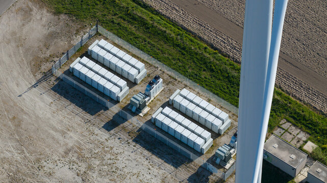Aerial view of a battery energy storage system with rows of white containers next to a wind turbine mast in Ooltgensplaat, Zuid-Holland, Netherlands.