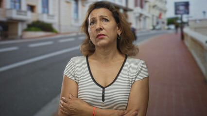 Woman crossing arms on city street near car wearing striped shirt and hoop earrings in summer  uncertainty. © Krakenimages.com