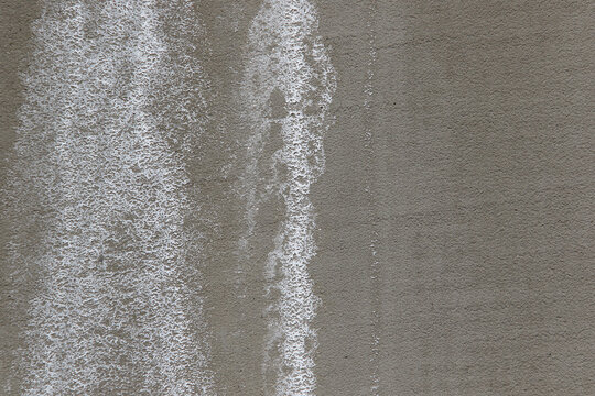 Close-up of white efflorescence salt deposits on a grey concrete wall.