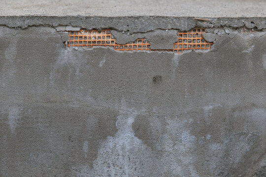 Cracked plaster on concrete wall with exposed orange reinforcing mesh and efflorescence.