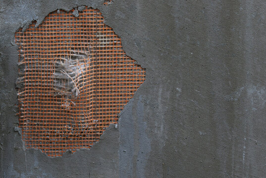 Cracked plaster on concrete wall with exposed orange reinforcing mesh and efflorescence.