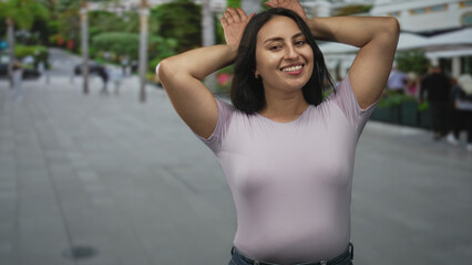 Woman waving right hand with raised arm on a busy city street plaza in front of outdoor cafes and planters  joy confidence. © Krakenimages.com